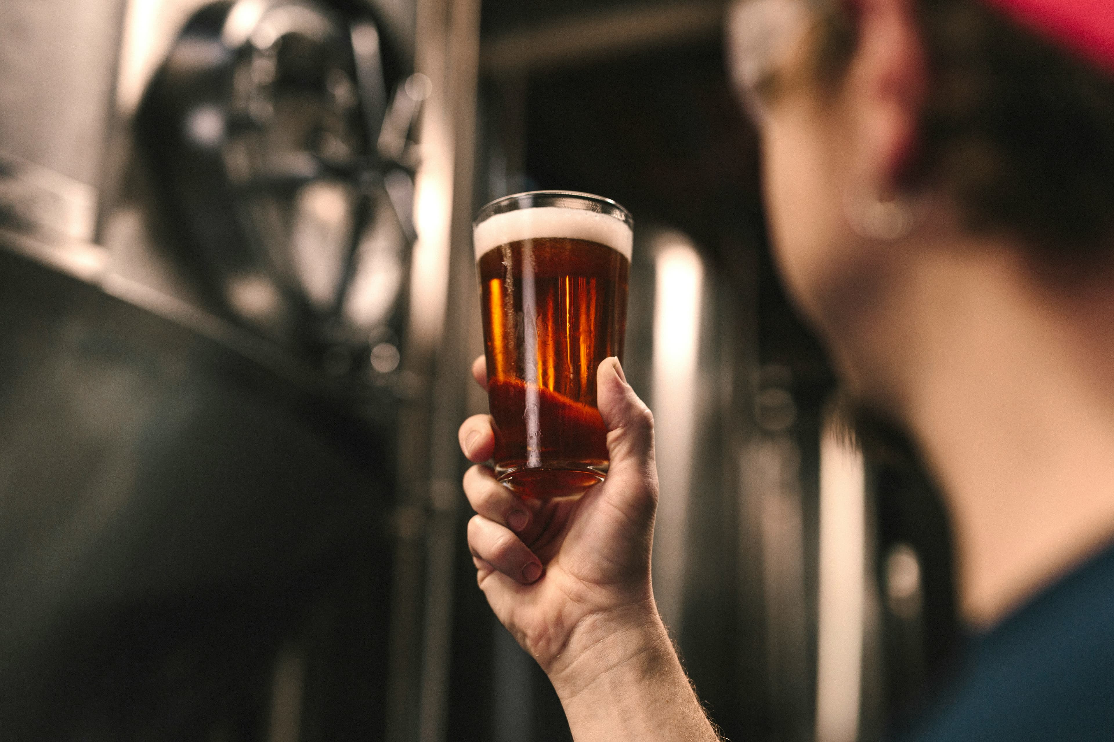 Beer brewers examining beer standing in front of brewing equipment